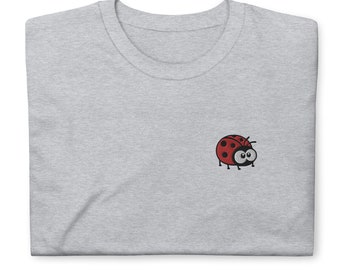 Puede incluir: Una camiseta gris con una mariquita roja y negra bordada en la parte delantera.