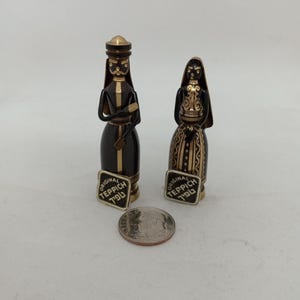 May include: Two small, dark-colored figurines with gold accents, resembling traditional figures. Each figurine has a label that reads "ORIGINAL TEPPICH". A US dime is included for size comparison. The figurines are on a white background.