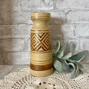 May include: A vintage ceramic vase with a tan and brown geometric design. The vase has a cylindrical shape with a wider base and top. The design features diamond patterns and horizontal stripes. The vase is approximately 8 inches tall.