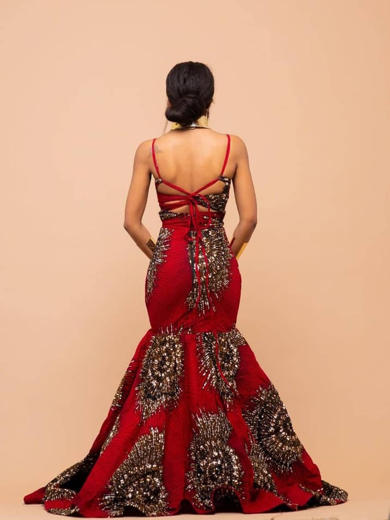May include: A red and gold mermaid-style gown with a low back and a lace-up detail. The gown is adorned with gold sequins and beads.