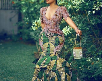 Pode incluir: Uma mulher vestindo um vestido estampado em verde e dourado com um corpete de contas rosa. Ela está segurando uma pequena bolsa de mão de contas.