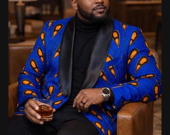 May include: A blue blazer with an orange and yellow pattern, black lapels, and a black turtleneck. The blazer is paired with black pants. The person is seated in a brown leather chair and holding a glass of amber liquid.