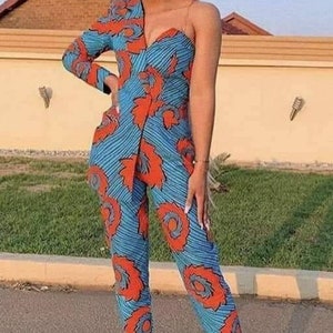 May include: A woman wearing a one-shoulder jumpsuit with a blue and orange patterned design. The jumpsuit has a fitted bodice and wide-leg pants.