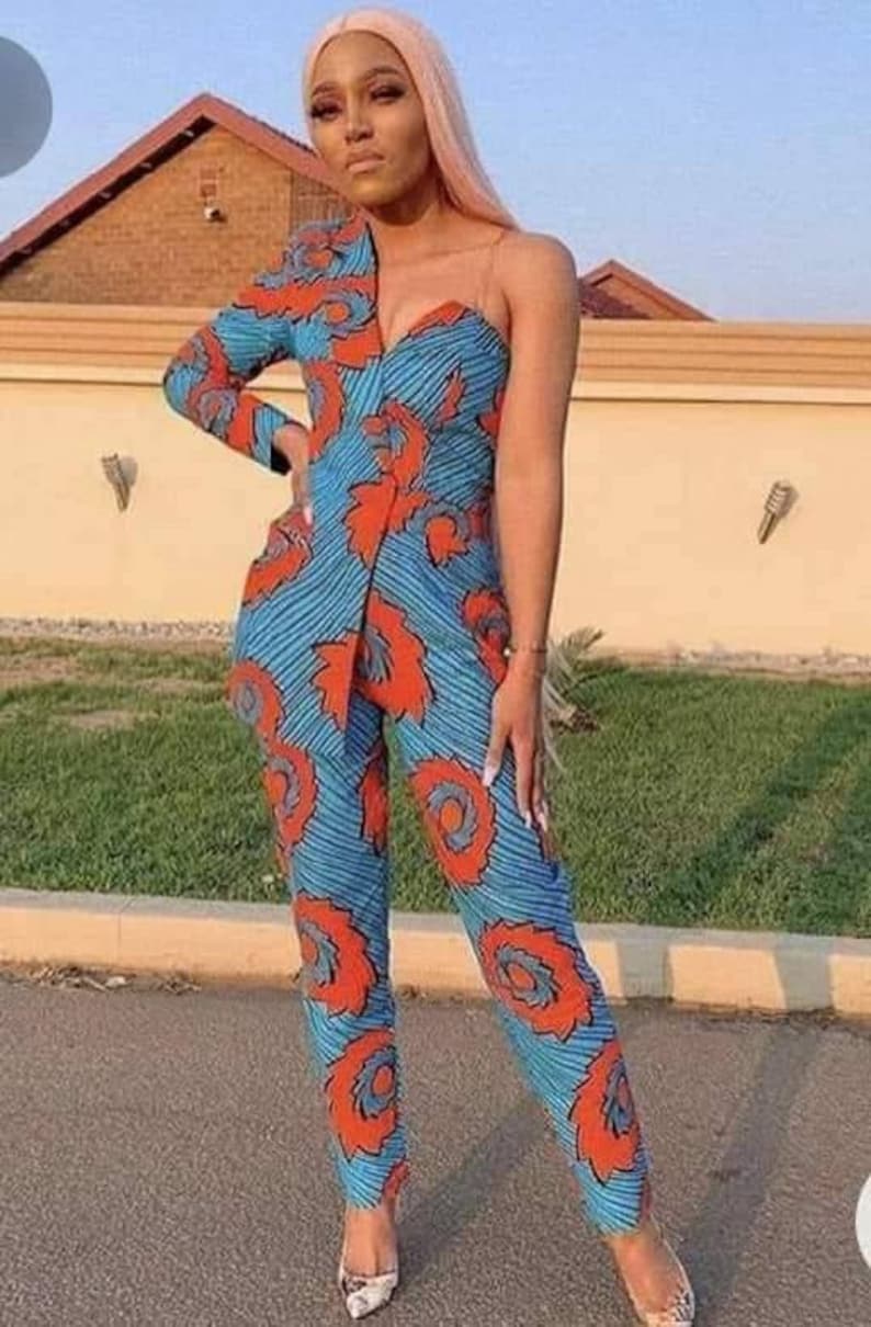 May include: A woman wearing a one-shoulder jumpsuit with a blue and orange patterned design. The jumpsuit has a fitted bodice and wide-leg pants.