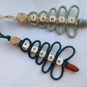 May include: Two personalised Christmas tree decorations with the names JAMIE and KEOGH spelled out with wooden letter beads. The decorations are made with green and white string and have wooden beads at the top.
