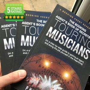 Puede incluir: Tres libros de bolsillo negros con el título "Agent's Book of Secrets Touring Musicians" y un subtítulo "(or, a step-by-step guide to getting an agent, and doing the job yourself in the meantime)". La portada del libro presenta un escenario de concierto con focos.