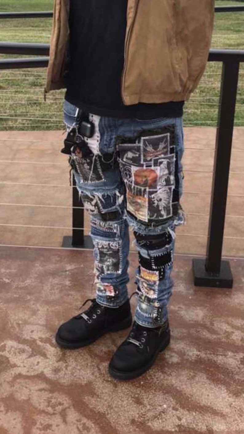 Puede incluir: Vaqueros azules con m&uacute;ltiples parches gr&aacute;ficos y detalles desgastados. Los vaqueros se combinan con zapatos negros. La persona lleva una chaqueta marr&oacute;n y una camiseta negra.
