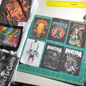 Puede incluir: Un conjunto de parches de bandas de m&uacute;sica, incluyendo Pantera, Metallica y Alice in Chains, con fondos negros y varios dise&ntilde;os gr&aacute;ficos. Algunos parches est&aacute;n sobre tela blanca. Tambi&eacute;n se ve una regla amarilla. Los parches est&aacute;n sobre una esterilla de corte verde.