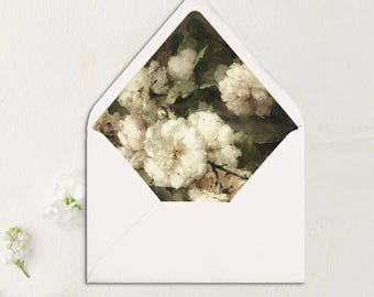Può includere: Busta bianca con un disegno floreale sulla lembo. Il disegno presenta fiori bianchi con foglie verdi su uno sfondo scuro.