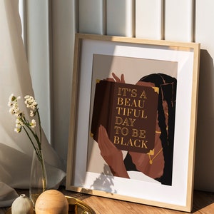 May include: A framed print with a brown background featuring a person holding a book with the text "It's a beautiful day to be black".