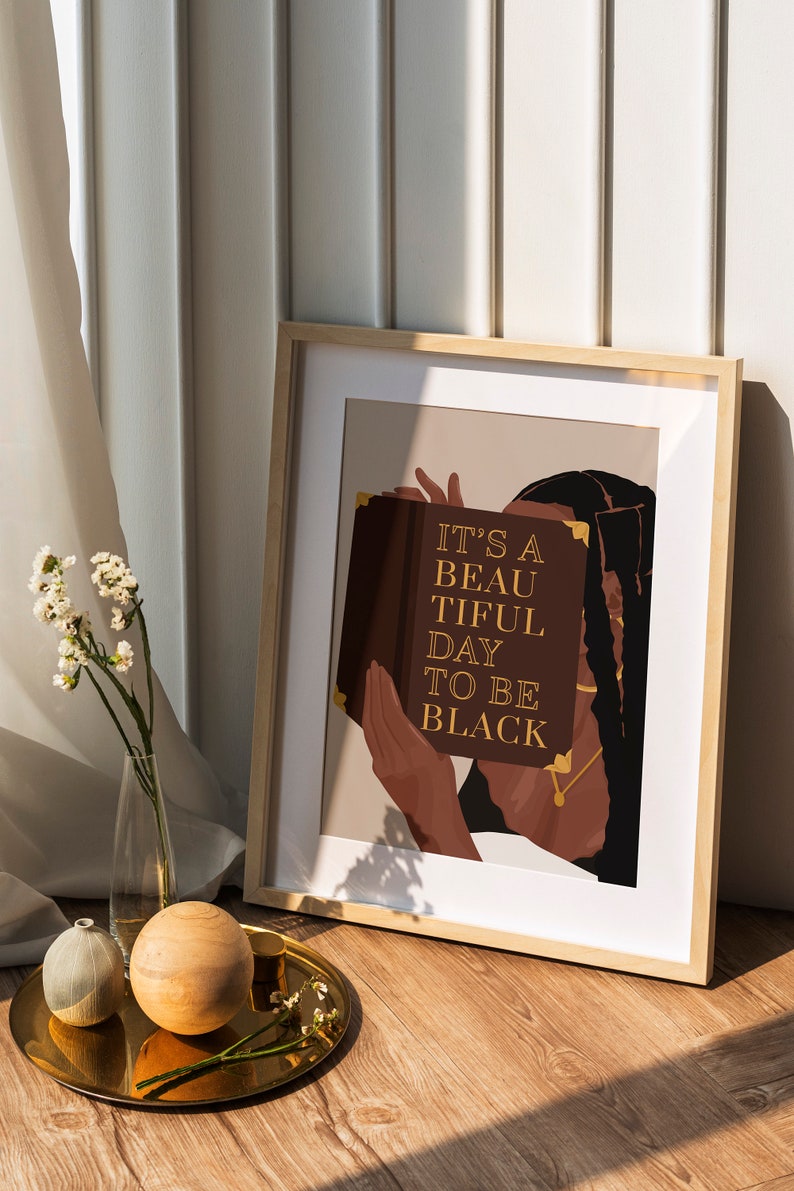 May include: A framed print with a brown background featuring a person holding a book with the text "It's a beautiful day to be black".