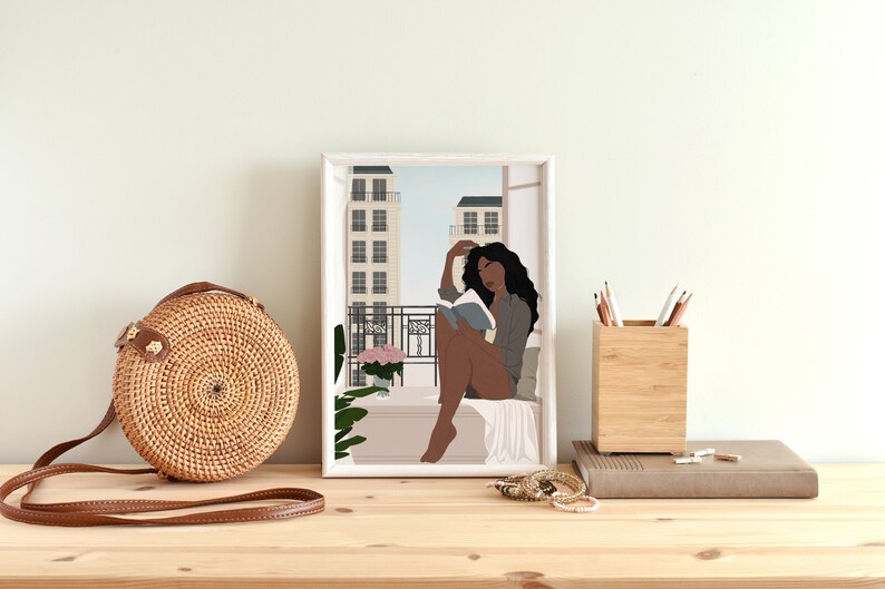 May include: A digital illustration of a Black woman sitting on a balcony, reading a book, with a view of city buildings in the background. The illustration is framed in a white frame.