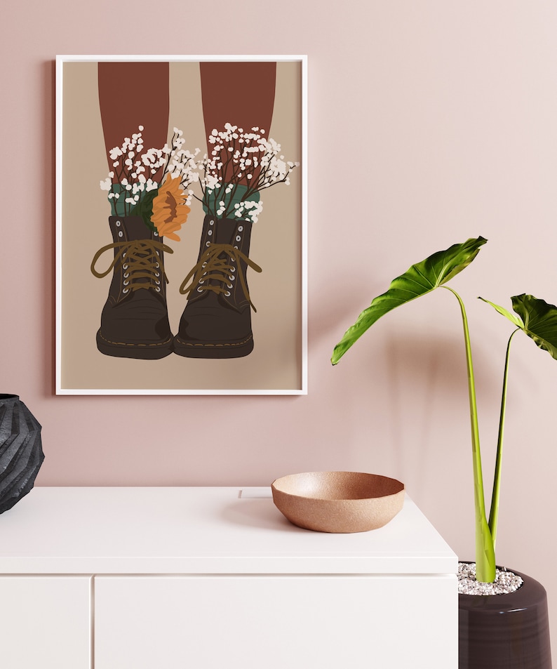 May include: A pair of brown leather boots with white flowers growing out of them. The boots are on a beige background.