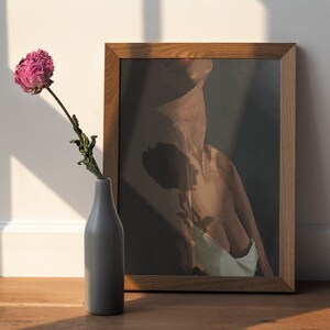 May include: A framed print of a nude figure with a dark background. A single dried pink peony flower in a gray vase sits in front of the print.
