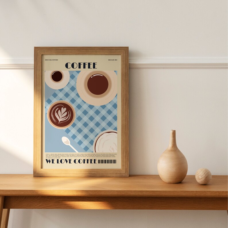 May include: A framed art print featuring coffee cups and the text "COFFEE" and "WE LOVE COFFEE." The artwork has a light blue checkered background and a light brown wooden frame. A wooden vase and ball sit on a wooden table.