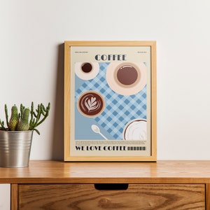 May include: A framed art print featuring coffee cups and a latte on a blue checkered background. The word "COFFEE" is at the top, and "WE LOVE COFFEE" is at the bottom. The print is displayed on a wooden surface.