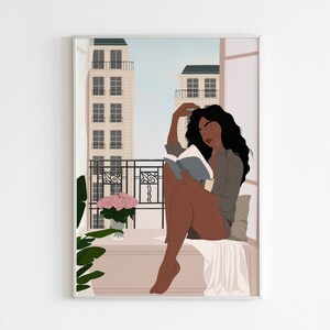 May include: A woman with long, dark hair sits on a balcony reading a book. She is wearing a gray shirt and has a white blanket draped over her legs. There are buildings in the background and a potted plant with pink flowers on the balcony.