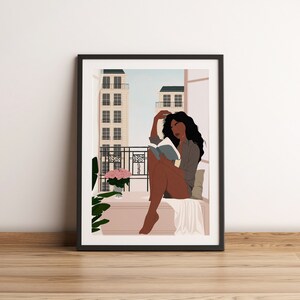 May include: A framed illustration of a woman sitting on a balcony reading a book. The woman has long dark hair and is wearing a gray shirt. The balcony has a view of a city with buildings in the background. There are pink flowers in a pot on the balcony.