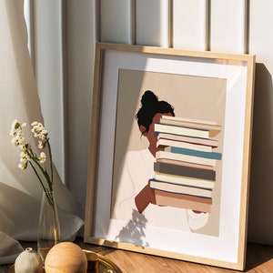 Peut inclure: Impression d'art encadr&eacute;e repr&eacute;sentant une personne tenant une pile de livres. L'illustration est minimaliste, avec une palette de couleurs neutres et un cadre en bois clair. L'image est pos&eacute;e sur un fond neutre.