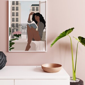 May include: A framed illustration of a woman sitting on a balcony reading a book. The woman has dark skin and long black hair. She is wearing a blue shirt and has a pink flower bouquet on the balcony.