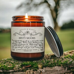 May include: A brown glass candle jar with a white label that reads "Belle & Happy Misty Moors". The label has a decorative floral design and text that reads "The air carried the smell of wild heather and wild. The moors. That's where Catherine and Heathcliff will forever be. "Make everything stop and stand still and never, never move again. Make the waves never change, and you and I never change." The candle is a coconut soy candle with a net weight of 8 oz or 226 grams. It is handmade in MI.