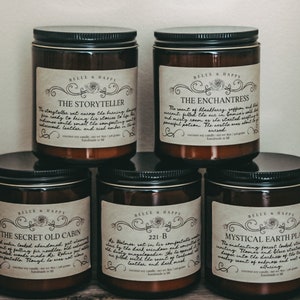 May include: Six amber glass candle jars with black lids and labels. The labels are cream colored with black text and feature different names for each candle: "The Storyteller", "The Enchantress", "The Secret Old Cabin", "221-B", "Mystical Earth Places".
