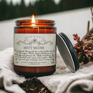 May include: A brown glass candle jar with a white label that reads "BELLE & HAPPY" and "MISTY MOORS". The label has a decorative floral design and the text "coconut soy candle net wt: 8oz / 226 grams handmade in MI".