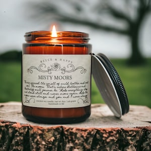 May include: A brown glass candle jar with a white label that reads "Belle & Happy Misty Moors". The label has a decorative floral design and text that reads "The air carried the smell of wild heather and wild wil. The moons. That's where Catherine and Hatheliff will forever be. "Make everything stop and stand still forever be. Move again. Make the waves never change, and you and I never change." The candle is 8 oz / 226 grams and is handmade in MI.