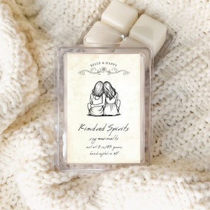 May include: A clear plastic container with a white label that reads "BELLE & HAPPY" and "Kindred Spirits soy wax melts net wt. 3 oz/85 grams handcrafted in US". The label features a black and white illustration of two women standing back to back with their arms around each other.