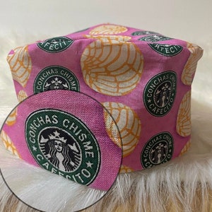 May include: Pink fabric with a repeating pattern of green and white "Conchas Chisme Cafecito" logos and yellow and white concha bread.