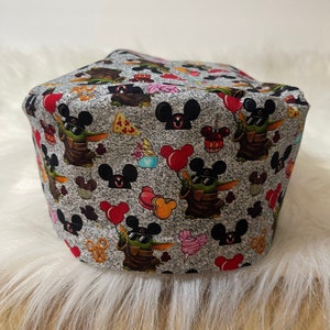 May include: A grey scrub hat with a repeating pattern of Mickey Mouse ears, red balloons, and a cartoon character with green skin and large ears. The character is wearing sunglasses and holding a red balloon.