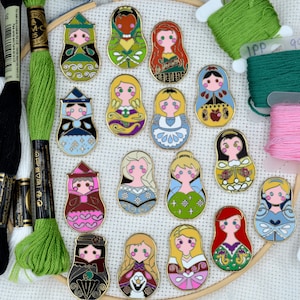 May include: A set of 16 Disney princess-themed nesting dolls, each featuring a different princess in a colorful, detailed design. The dolls are arranged in a circle on a white fabric background.