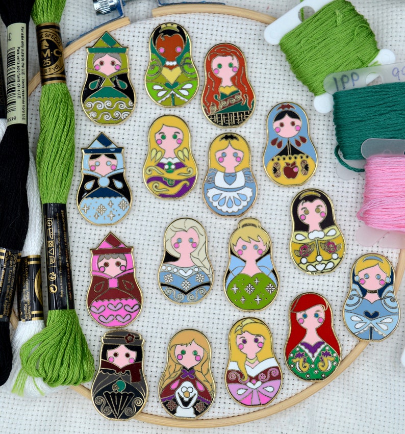 May include: A set of 16 Disney princess-themed nesting dolls, each featuring a different princess in a colorful, detailed design. The dolls are arranged in a circle on a white fabric background.