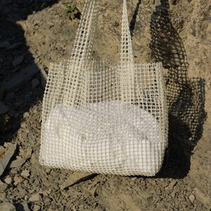 May include: A white mesh tote bag with a white fabric lining. The bag is made of a durable, lightweight material and has a spacious interior.