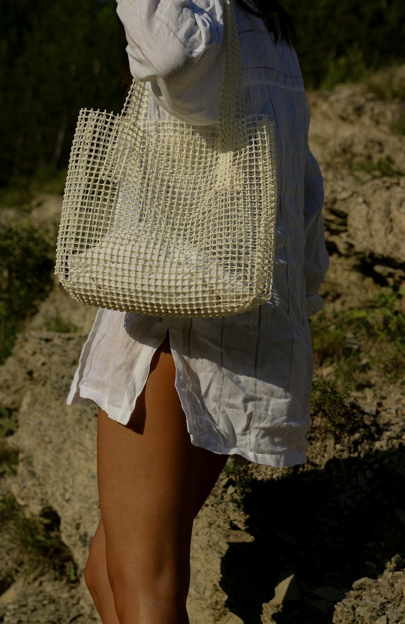 May include: A white mesh tote bag with a white shirt. The bag is being held by a person.