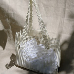 May include: A white mesh tote bag with a white fabric lining. The bag is made of a durable, lightweight material and has a spacious interior.