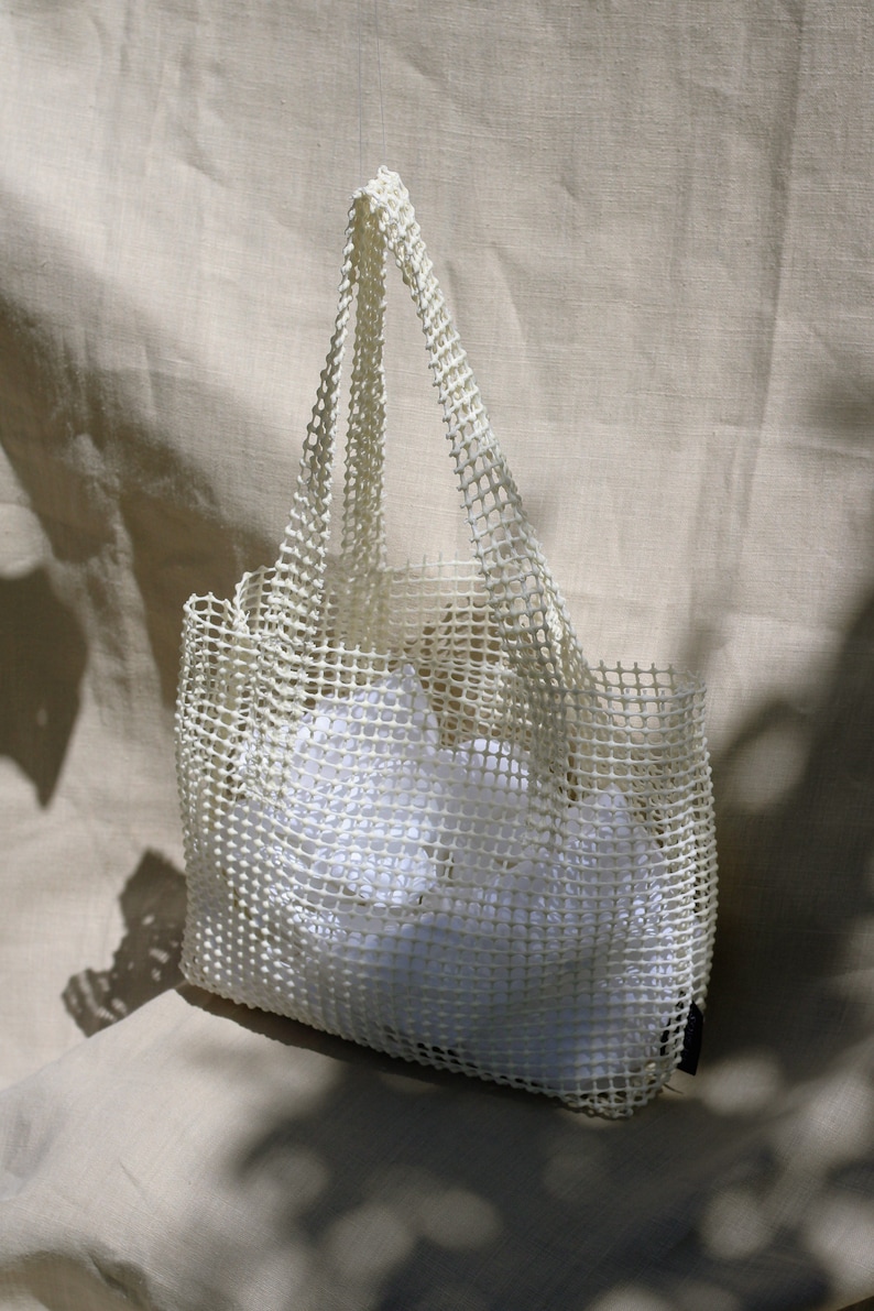 May include: A white mesh tote bag with a white fabric lining. The bag is made of a durable, lightweight material and has a spacious interior.