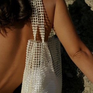 May include: A white mesh tote bag with a wide, flat base and two straps. The bag is made of a woven material with a grid pattern.