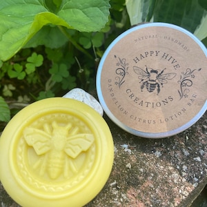 May include: A yellow, round, solid lotion bar with a bee design. The bar is labeled "Happy Hive Creations Citrus Lotion Bar" and "Natural Handmade".