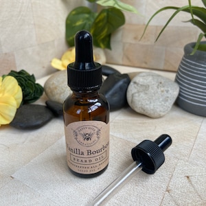 May include: A brown glass bottle with a black dropper top and a label that reads "Happy Hive Creations Vanilla Bourbon Beard Oil Handcrafted All Natural Green Bay, WI".