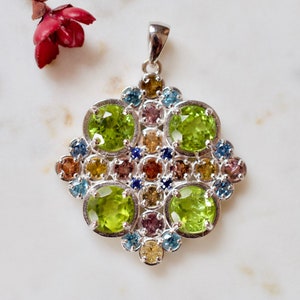 May include: A silver pendant with a cluster of green, blue, and brown gemstones. The pendant is in the shape of a flower with a square center.