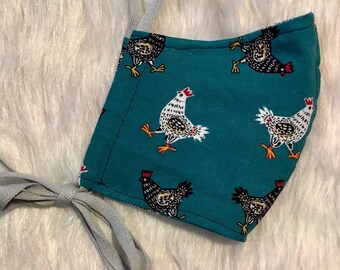 May include: A teal blue fabric face mask with a white string. The mask has a repeating pattern of black and white chickens.