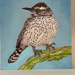 May include: A painting of a brown and white bird perched on a green cactus with a blue background. The bird has a long, pointed beak and a spotted pattern on its feathers. The artist's signature, "Vines", is in the bottom right corner.
