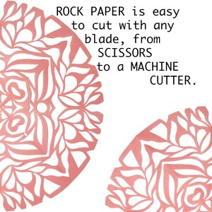 May include: Two pink paper cutouts of intricate designs with the text "ROCK PAPER is easy to cut with any blade, from SCISSORS to a MACHINE CUTTER."