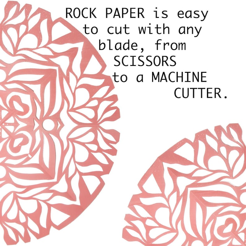 May include: Two pink paper cutouts of intricate designs with the text "ROCK PAPER is easy to cut with any blade, from SCISSORS to a MACHINE CUTTER."