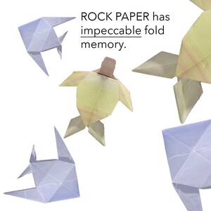May include: Four origami figures, a turtle, two fish, and a whale, made of paper in shades of blue and yellow. The text "ROCK PAPER has impeccable fold memory." is written above the figures.