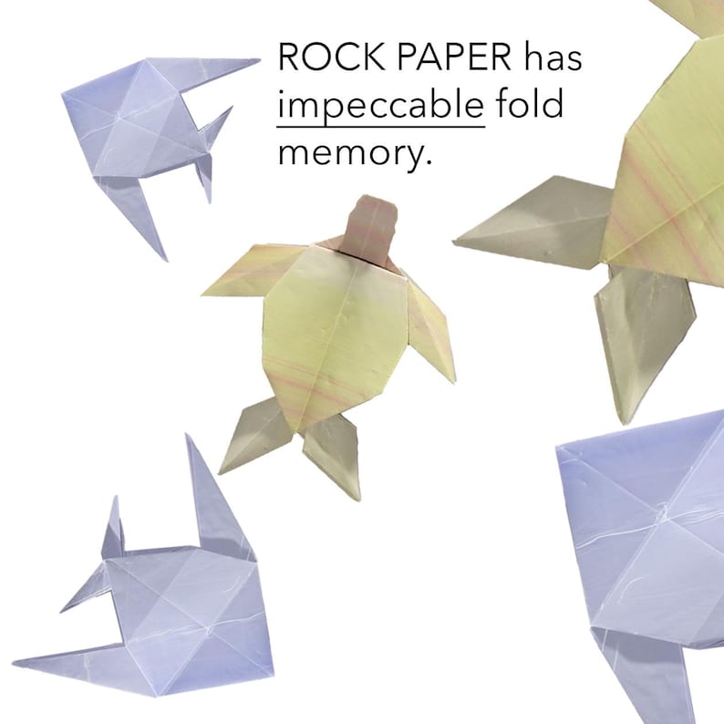 May include: Four origami figures, a turtle, two fish, and a whale, made of paper in shades of blue and yellow. The text "ROCK PAPER has impeccable fold memory." is written above the figures.