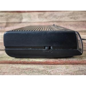 K&ouml;nnte beinhalten: Ein schwarzes Vintage-Digital-Radiowecker mit gerippter Oberseite und einem Dimmschalter. Der Radiowecker hat eine rechteckige Form und eine transparente Kunststofffront. Das Wort "DIMMER" ist unten aufgedruckt.