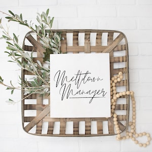 Puede incluir: Un letrero cuadrado blanco con caligrafía negra que dice "Meltdown Manager" en una caja de madera rústica con una hebra de cuentas de madera.
