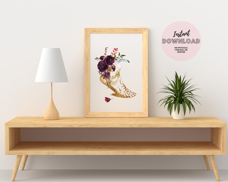 Pu&ograve; includere: Un download digitale stampabile di una luna crescente dorata con fiori viola e piume. L'immagine &egrave; incorniciata ed esposta su uno scaffale con una lampada e una pianta in vaso.